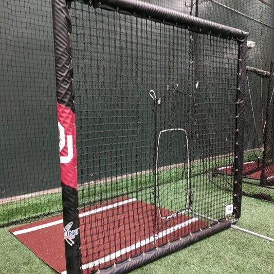 A baseball field with a batting cage and green wall.