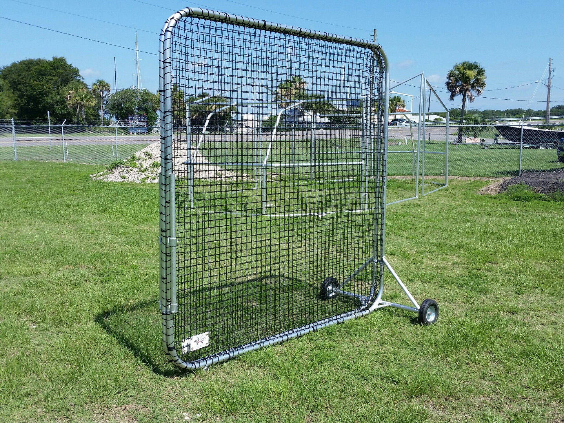 A baseball screen on wheels in the grass.