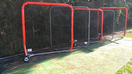 A baseball field with red poles and black net.