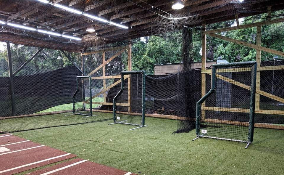 A baseball field with batting cages and a net.