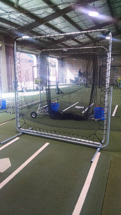 A baseball catcher is laying in the middle of his cage.