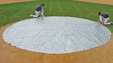 A man kneeling down on the ground in front of a tarp.