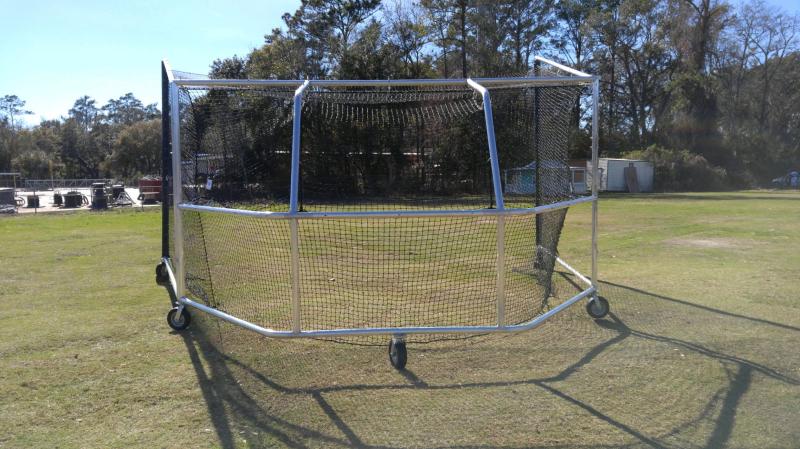 A baseball cage on wheels in the middle of a field.