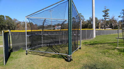 A baseball cage on the grass near a fence.