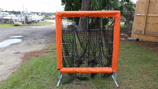 A baseball net in the grass near a tree.