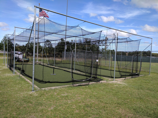 A baseball field with a batting cage and american flag.